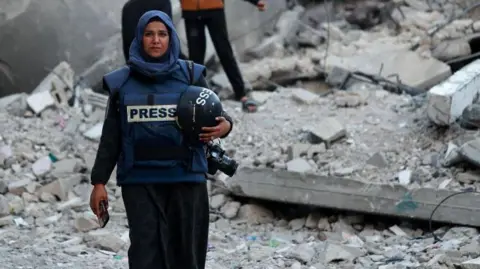 Anadolu via Getty Photojournalist Doaa Albaz is photographed in the ruins of Rafah City, rubble all around her.