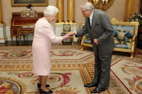 Getty Images David Hockney and HM Queen Elizabeth II. Hockey is bowing and has taken the late Queen's hand. They are in a palace.
