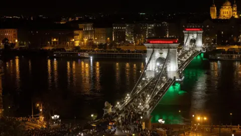 EPA Crowds walking across the Chain Bridge as it's illuminated in green, red and white lights during the night of the general elections in Budapest