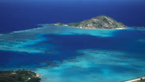 Getty Images An aerial shot of Lizard Island - a small island on Australia's Great Barrier Reef - showing the calm blue shallow waters of the reef. The island is dominated by a peak.