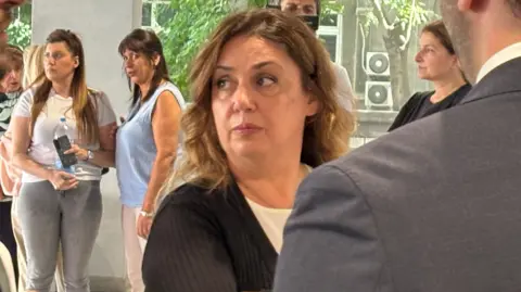 Slobodan Maricic/BBC Serbian A woman in a cardigan looks on with a worried expression while a man in a grey suit has his back to the camera