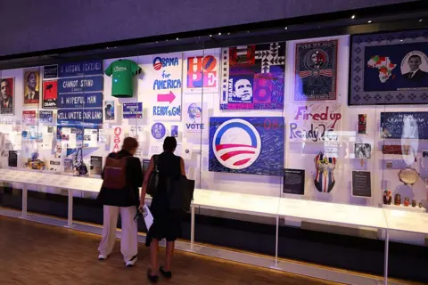 Talia Sprague/Bloomberg via Getty Images People stand and look at an exhibit of campaign merchandise and supporter-made memorabilia from Obama's presidential campaigns.