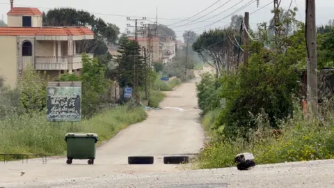 Neha Sharma/BBC A large rubbish bin and two tyres on an empty road in southern Lebanon, near territory occupied by Israeli forces