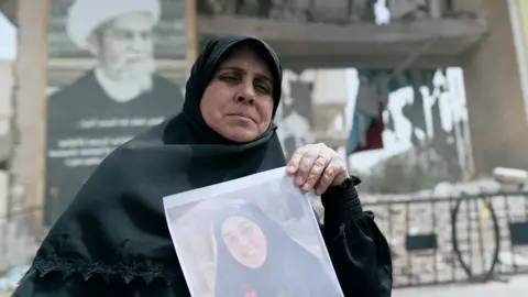 Veiled woman holds up portrait of one of her dead daughters