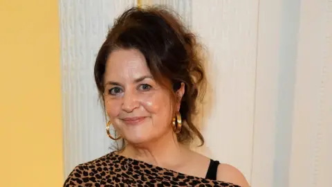 PA Media Close-up of Ruth Jones. She wears her brown hair up. She has gold hoops, and wears an off-shoulder leopard print dress.