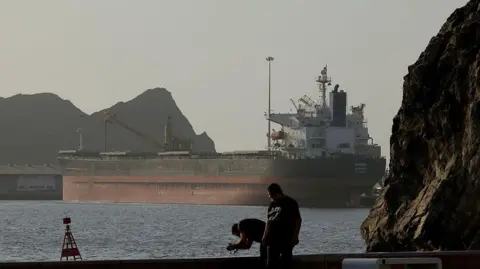 Anadolu via Getty Images An oil tanker stands anchored between two rocky shores on a sunny evening. The image shows the Strait of Hormuz on 17 June