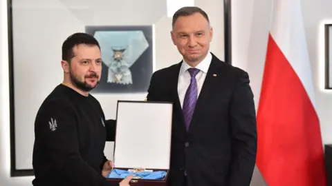 EPA-EFE/REX/Shutterstock Polish President Andrzej Duda (R), wearing a suit and tie, awards Ukrainian President Volodymyr Zelensky, wearing a black-long sleeve shirt, with the Order of the White Eagle during his visit in Warsaw, Poland. The medal is lying in an opened box, which Zelensky is holding.