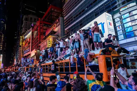 Getty Images Dozens of people stand on top of a school bus parked in Manhattan, as others climb onto the vehicle.