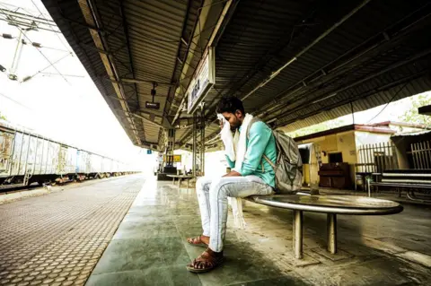 Ankit Srinivas A man sits and wipes his forehead with a white cloth on a deserted railway platform at Banda