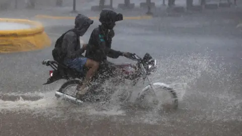 EPA Two people ride a motorcycle through deep rainwater in the Dominican Republic.