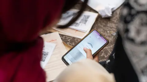 NurPhoto / Getty Images A woman in a red headscarf looks at a phone which is running a VPN app
