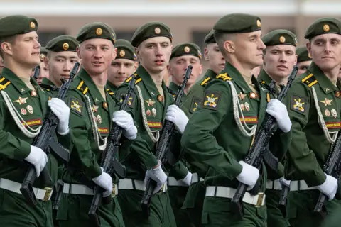 Getty Images Russian soldiers rehearse for parade on Red Square - they are in uniform, holding automatic weapons with white gloves, marching left to right and looking towards the camera.