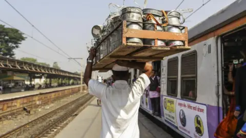 Bloomberg via Getty Images Dabbawala Dasharath Kedari carries a crate of tiffin boxes while walking past a train at the Santacruz railway station in Mumbai, India