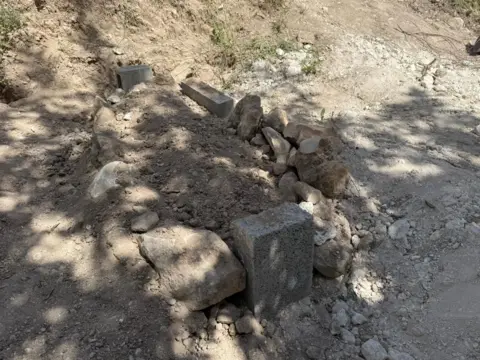 A newly dug grave, with dirt in the centre surrounded by rocks of varying sizes.