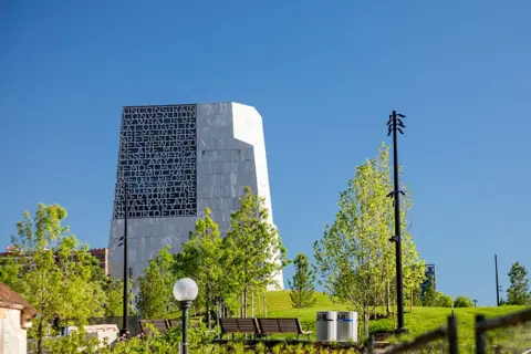 Universal Images Group via Getty Images The Obama Presidential Center, a large modern stone building, rises over a lush green park and benches in Chicago.