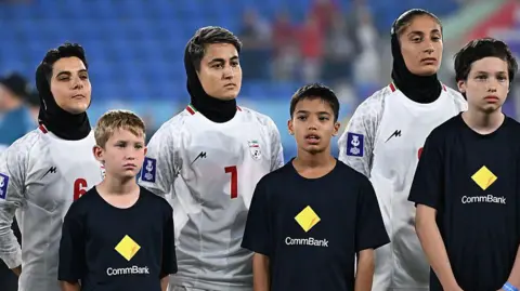 Getty Three women wear white football jerseys and black headscarves while three boys in black t-shirts stand in front of them