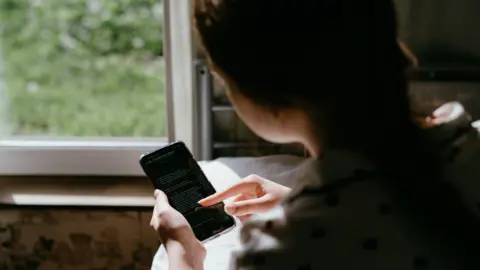 Getty Images An over the shoulder shot of a young girl scrolling on a phone screen