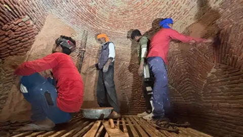 Aman/BBC Four men put the mortar on walls of the royal kitchen - which has sandstone bricks visible - as part of the restoration. 