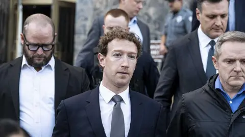 Getty Images Mark Zuckerberg, wearing a navy suit and grey tie, leaving court in Los Angeles in February, flanked other personnel.