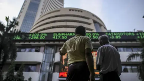 Dhiraj Singh/Bloomberg via Getty Images Pedestrians look up at an electronic screen and a digital ticker board at the Bombay Stock Exchange (BSE) building in Mumbai. 