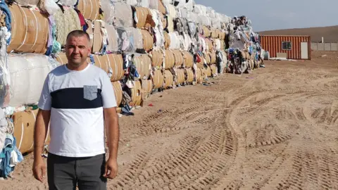 Bekir Conkur standing in front of bales of used clothing