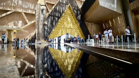 Reuters People walk next to a statue of King Ramses II in the main hall of the Grand Egyptian Museum, one of the country's most iconic monuments