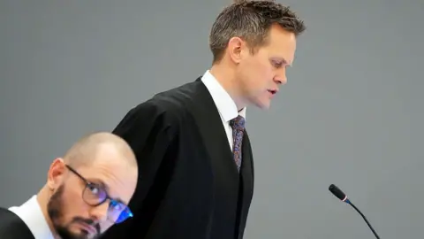 AFP via Getty Images A man in a gown and tie speaks in front of a microphone