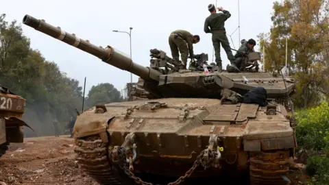 Reuters Israeli soldiers stand on top of a tank in northern Israel, near the Israel-Lebanon border. the tank is an imposing presence, taking up most of the frame.