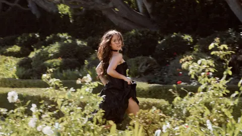 Emma Craft A picture of Laufey running through an ornate garden in a black ballgown