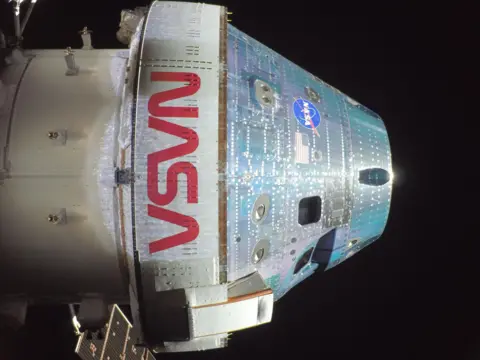 NASA A white cylindirical spacecraft in the blackness of space. Nasa is wriotten in large letters on its side