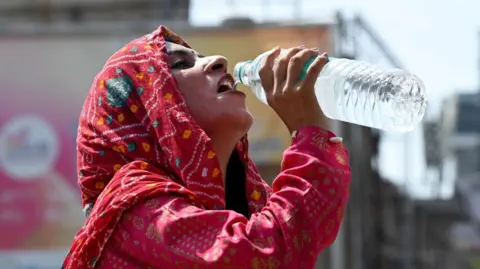 Getty Images A woman drinks from a bottle of packaged water on a hot day in India.