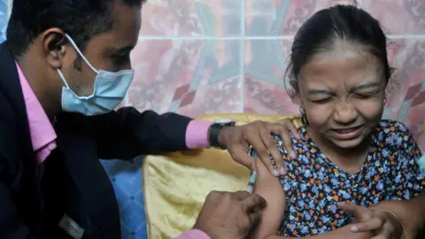 Getty Images A man inserting the needle of a syringe into the arm of a young girl.