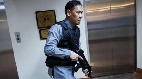 Reuters A man dressed in a blue shirt and a bullet-proof vest carrying a gun.