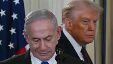 AFP via Getty Images Donald Trump stands behind Benjamin Netanyahu, who is looking downwards, during a press conference at the White House in 2025.