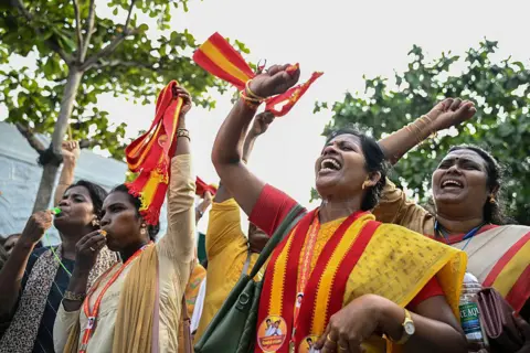 AFP via Getty Images Supporters and members of Indian actor C. Joseph Vijay's Tamilaga Vettri Kazhagam (TVK) party celebrate after TVK leads in the vote counting for the Tamil Nadu Legislative Assembly elections in Chennai on May 4, 2026. Women wear symbols of the party as they raise their hands in celebration.