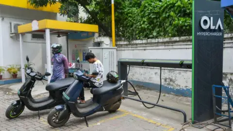 NurPhoto via Getty Images People are seen charging their electric scooters at An OLA electric vehicle hyper charging station in Kolkata , India. 