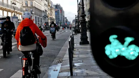 A cyclist in an orange top enjoys a cycle lane on a Paris street