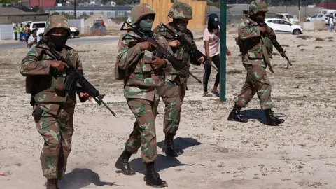 AFP via Getty Images Four uniformed soldiers are seen walking through a Cape Town township as part of their deployment to the area