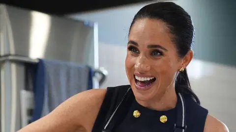 Getty Images Meghan Markle wearing a sleeveless black dress and apron