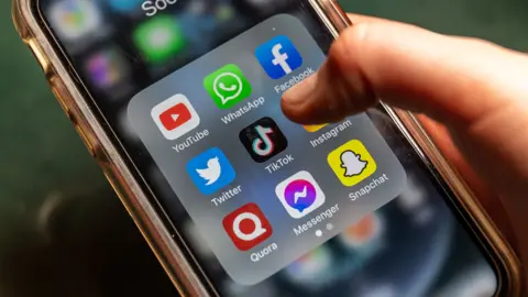 Getty Images A phone screen showing several social media platforms with someone's finger hovering over TikTok icon