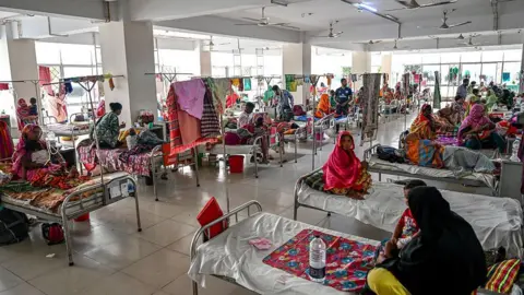 Getty Images A crowded hospital ward with women sitting cross-legged on their beds with colourful blankets. Some of the women have children