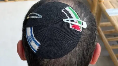 Alex Sinclair Top view of a man's head with a kippah embroidered with an Israel flag and a Palestinian flag