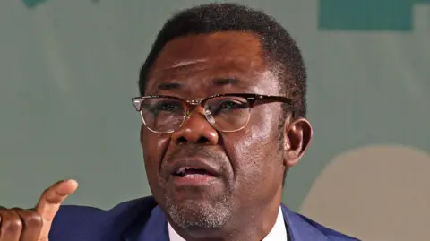 AFP via Getty Images A close up shot of Veron Mosengo-Omba talking. He wears glasses and a blue suit.
