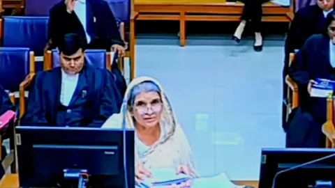 A woman wearing a white sari and flanked by lawyers deposing in a court in the Indian state of Madhya Pradesh