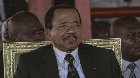 AFP via Getty Images Paul Biya wearing a dark suit and tie sitting in a gold-backed chair. 