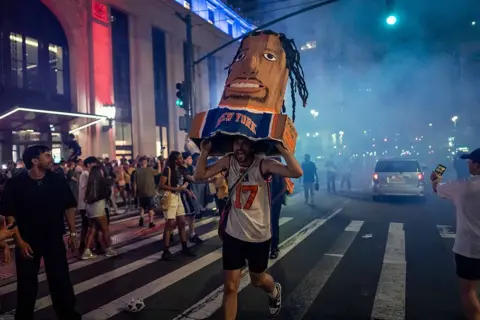 Getty Images A fan runs in the street holding a cardboard sculpture of a New York Knicks player's head and torso. 