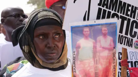 AFP via Getty Images A woman holds up a poster of victims of Yahya Jammeh's regime during a protest in 2020 calling for him to be brought to justice 2020. 