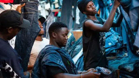 AFP via Getty Images Three vendors handle jeans at a market stall