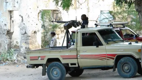 Getty Images A pick-up truck is parked by a bullet-marked wall. A large machine gun is mounted on the vehicle and someone is holding the trigger.