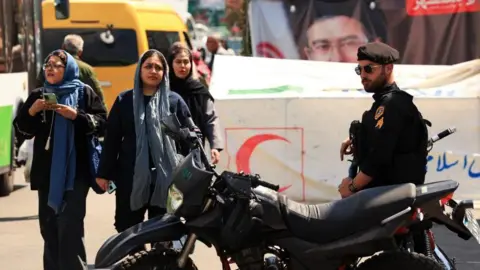Reuters Iranian women walk past a police officer standing guard on a street, amid a ceasefire between the U.S. and Iran, at Tajrish Square in Tehran